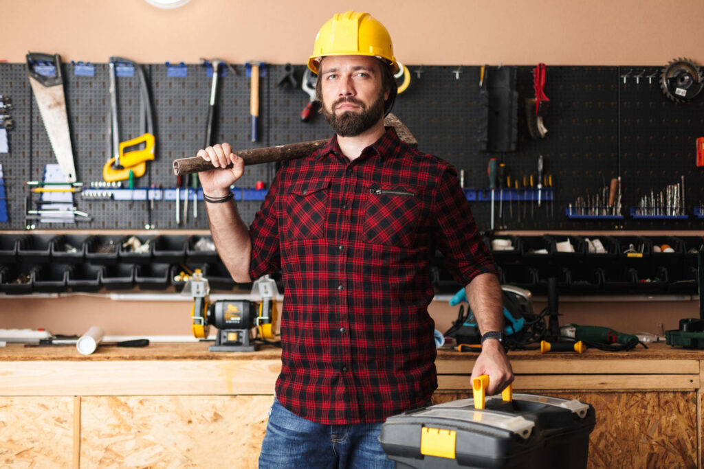 A professional, smiling handyman in a clean uniform holding a toolkit, standing in front of a well-maintained home — trustworthy and approachable.